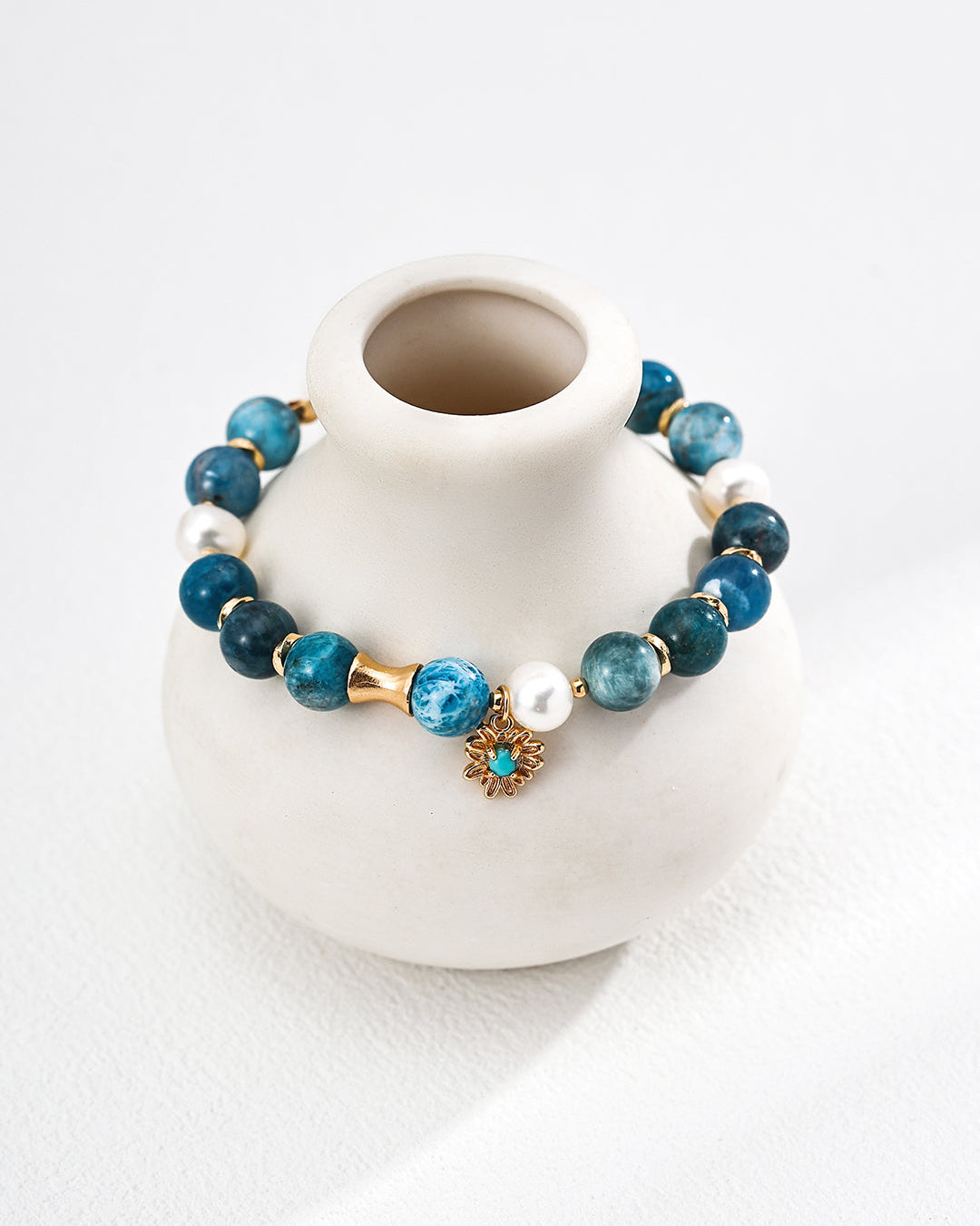 Blue beaded bracelet with a gold charm on a white vase against a white background